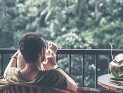 Ein Mann sitzt auf einem Balkon ohne Handy, neben sich eine offene Kokosnuss.