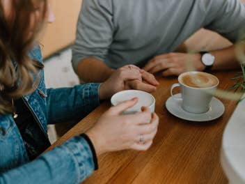 Ein Mann und eine Frau halten an einem Tisch bei einem Date Händchen, zwischen ihnen Kaffeetassen.