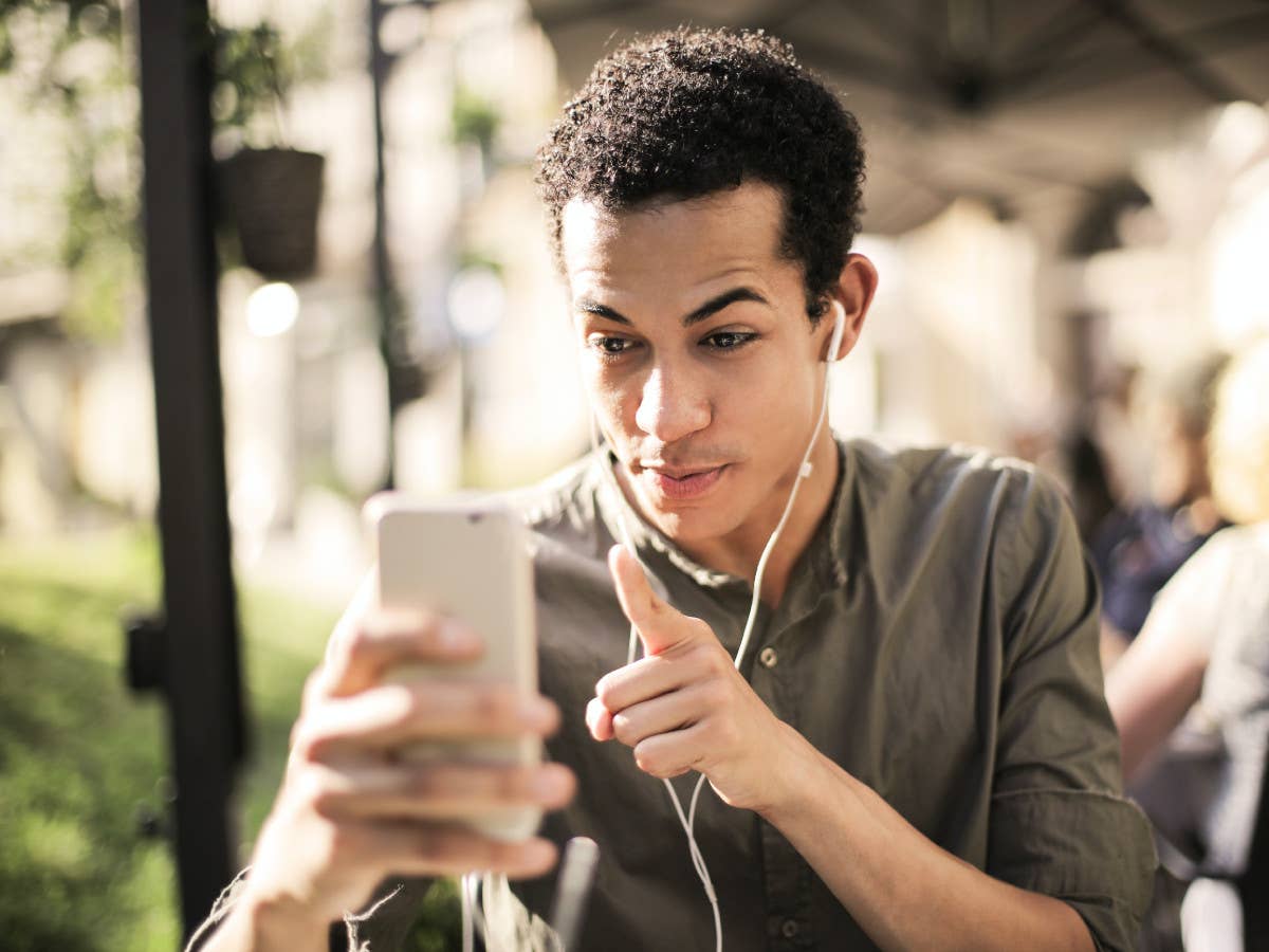 Ein junger Mann mit schwarzen Locken redet auf sein Smartphone ein und hat Kopfhörer in den Ohren