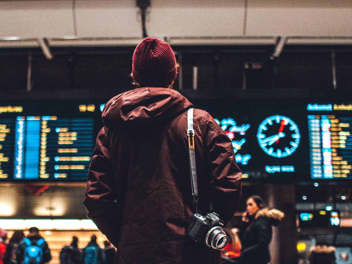 Mann steht im Flughafen und betrachtet die Abfluftafel