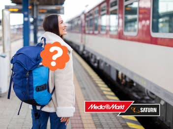 Eine Frau mit Rucksack steht am Bahngleis und schaut auf einen Zug. An ihrem Rucksack befindet sich ein Fragezeichen.