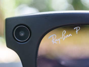 Nahaufnahme der oberen Ecke einer schwarzen Ray-Ban-Smart-Glasses, auf der das kreisrunde Kamera-Objektiv im Rahmen sowie der Schriftzug 