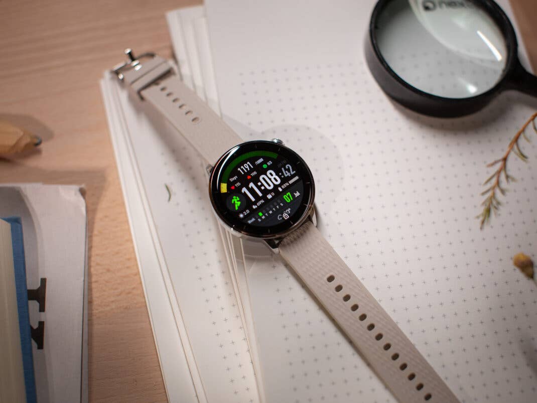 Eine OnePlus Watch 3 (43 mm) mit einem digitalen Display, das die Uhrzeit und Fitnessdaten auf einem Notizbuch anzeigt.