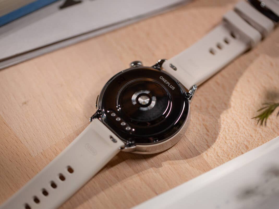 Rückansicht der OnePlus Watch 3 (43 mm) mit einem weißen Armband auf einer Holzoberfläche.