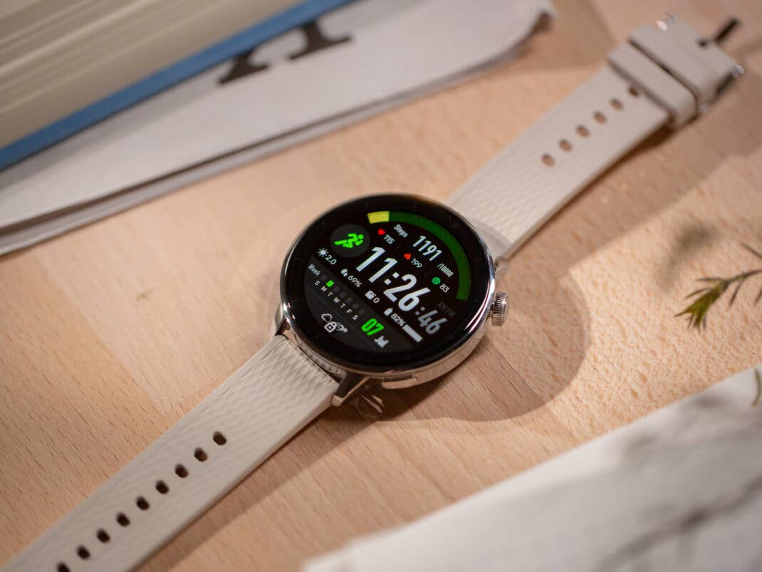 OnePlus Watch 3 mit rundem Display, das Fitnessstatistiken auf einer Holzoberfläche anzeigt.