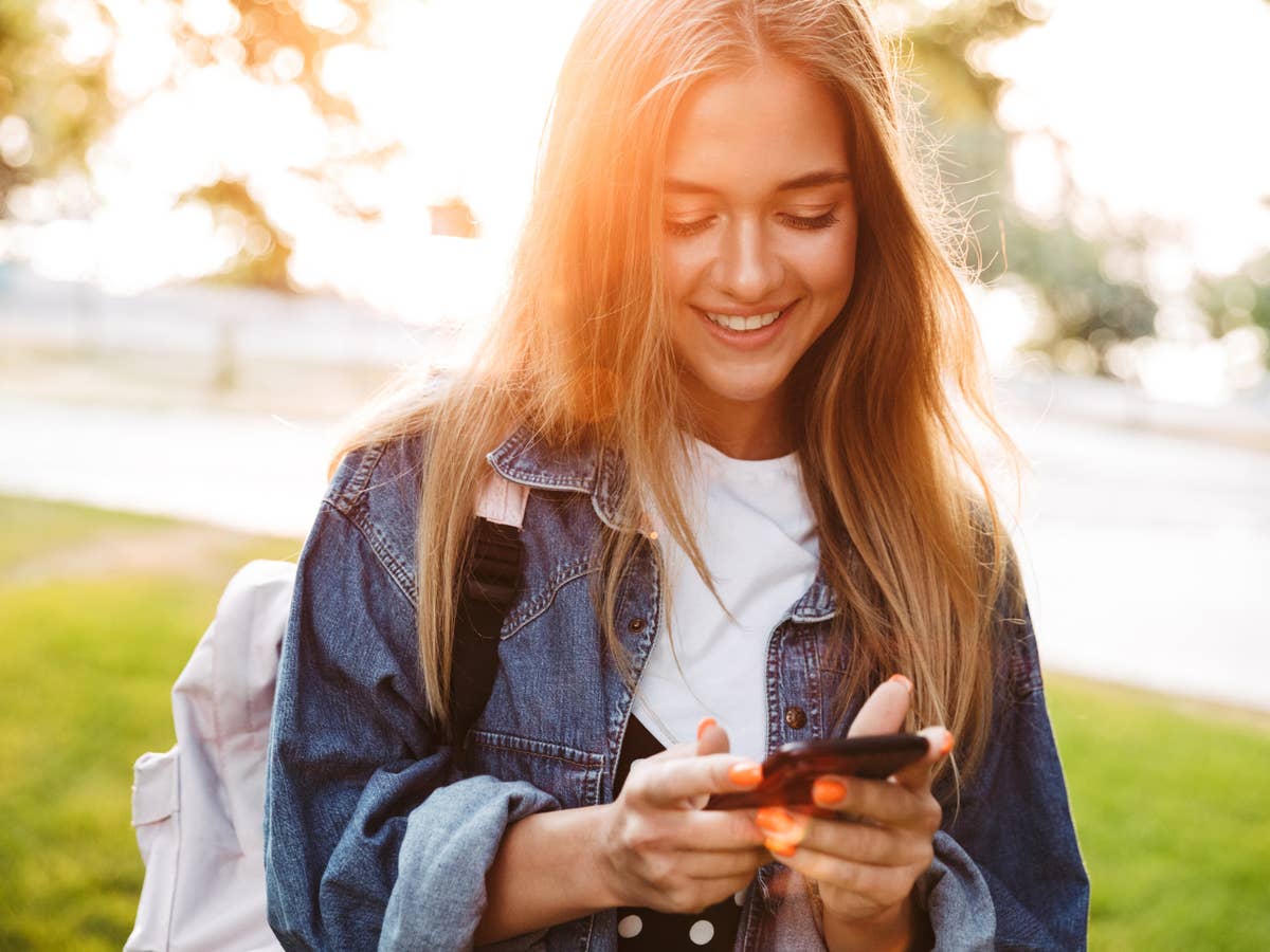 Junge Frau nutzt ein Smartphone und lächelt dabei.