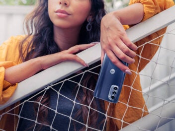 Frau lehnt über einem Zaun mit dem Motorola Moto G52 in der Hand.