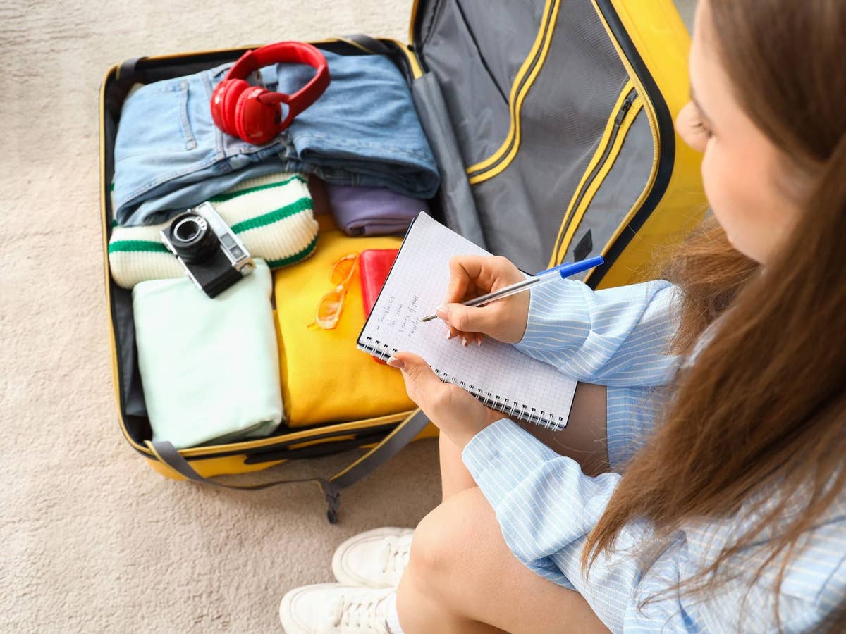 Must-haves für den Sommerurlaub Eine Frau packt einen Koffer und streicht etwas auf ihrer Packliste durch