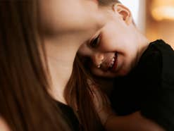 Kind kuschelt sich lachend an den Hals seiner Mutter.