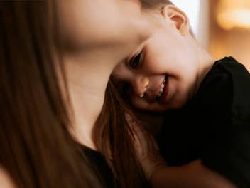 Kind kuschelt sich lachend an den Hals seiner Mutter.