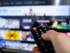 Nahaufnahme einer Fernbedienung die auf einen TV gerichtet ist