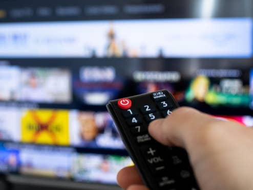 Nahaufnahme einer Fernbedienung die auf einen TV gerichtet ist