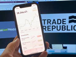 Smartphone mit geöffneter Trade Republic App vor Just Trade und Trade Republic Logo auf einem Monitor.
