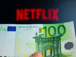 Netflix-Logo auf TV, davor eine Hand, die einen 100-Euro-Schein hält