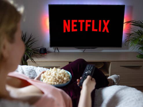 Frau sitz mit Popcorn und Fernbedienung auf der Couch und schaltet Netflix auf ihrem TV ein.