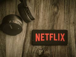 Netflix-Logo auf einem Smartphone, das neben Kopfhörern liegt.