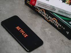 Das Netflix-Logo auf einem Smartphone, das auf einem Tisch neben Büchern liegt.