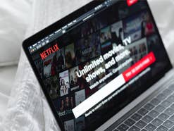 Netflix Startseite auf einem Laptop, der auf weißer Bettwäsche steht.
