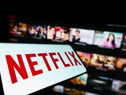 Netflix-Logo auf einem Smartphone vor Netflix-Homepgae im verschwommenen-Hintergrund.