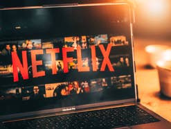 Netflix Logo auf einem Notebook-Displays vor warmem Licht einer Schreibtischleuchte.