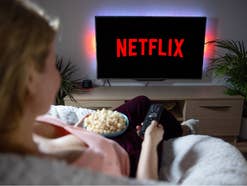 Eine Person sitzt mit Popcorn vor dem Smart TV, auf dem das Netflix-Logo eingeblendet ist.