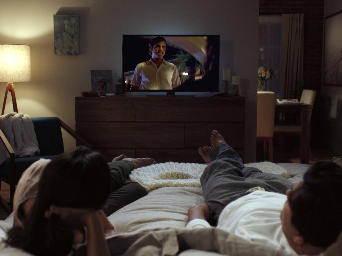 Ein Paar liegt auf dem Bett und schaut eine Serie auf dem Fernseher
