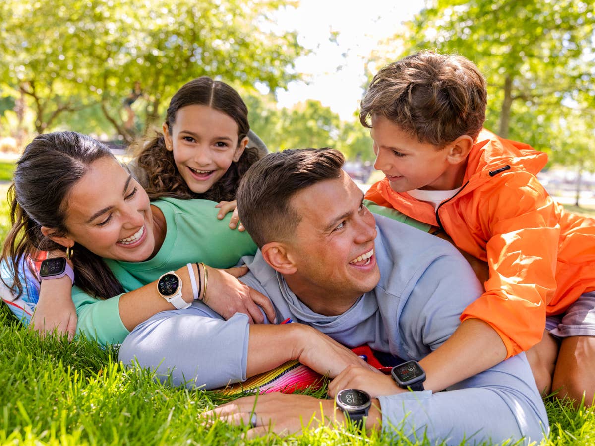 Familie liegt auf dem Rasen und freut sich über Smartwatches am Handgelenk.