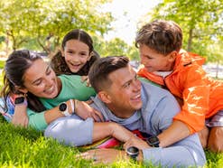 Familie liegt auf dem Rasen und freut sich über Smartwatches am Handgelenk.