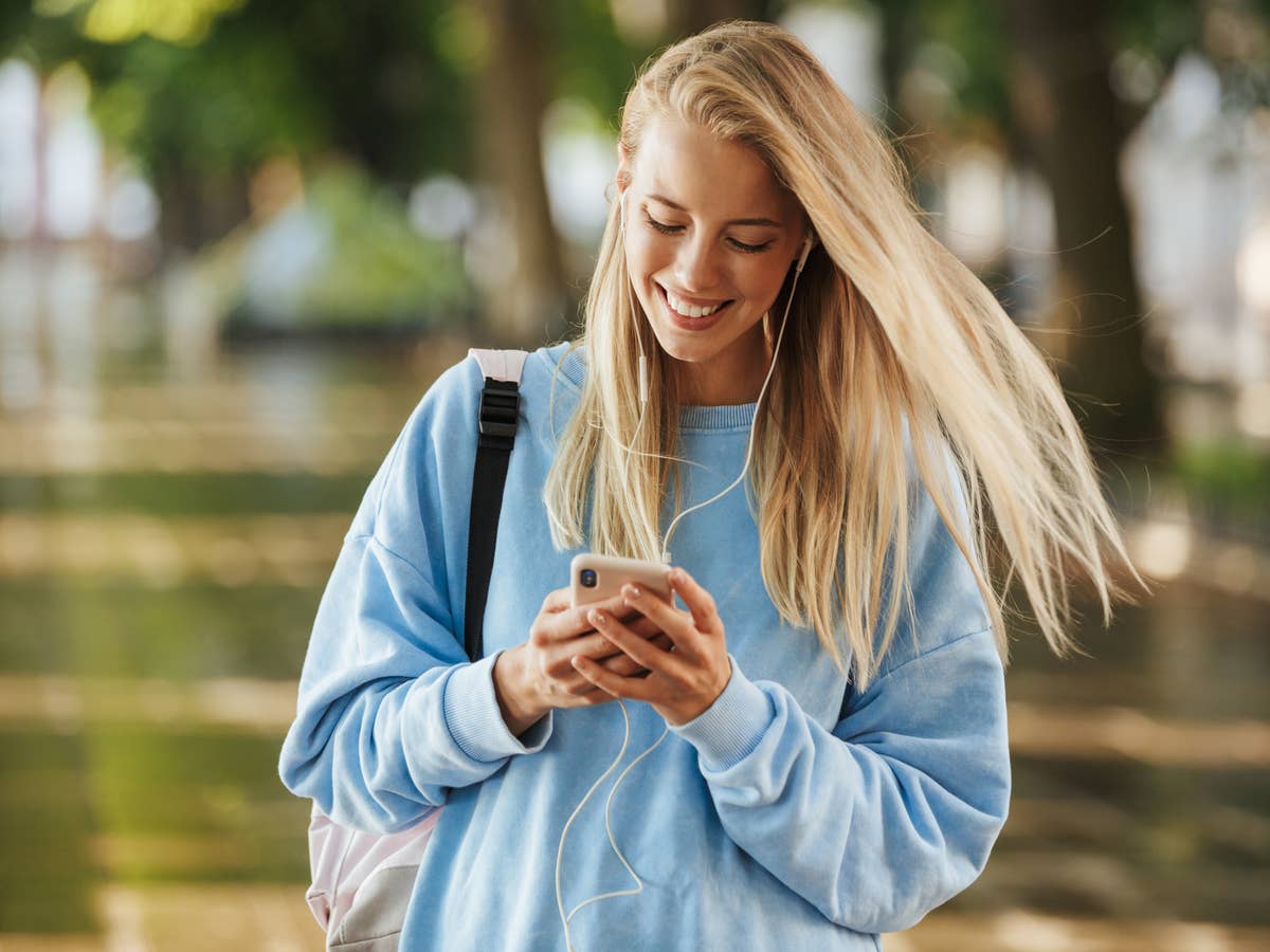 Junge blonde Frau hört über ein Smartphone Musik.