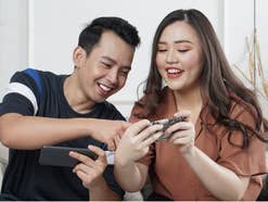 Zwei asiatische Menschen nutzen Smartphones auf einem Sofa.