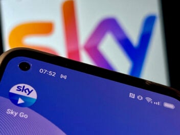 Sky Go auf einem Smartphone vor einem verschwommenen Sky Logo im Hintergrund.