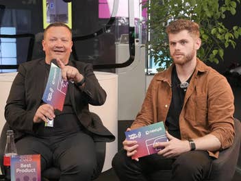 Zwei Männer sitzen in Stühlen auf der IFA, halten Auszeichnungen und diskutieren, mit Pflanzen im Hintergrund.