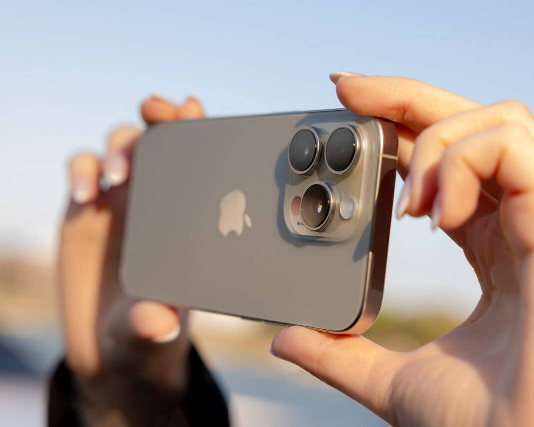 Eine Person hält ein iPhone 16 Pro, zeigt die Rückkamera und das Apple-Logo vor einem verschwommenen Hintergrund.