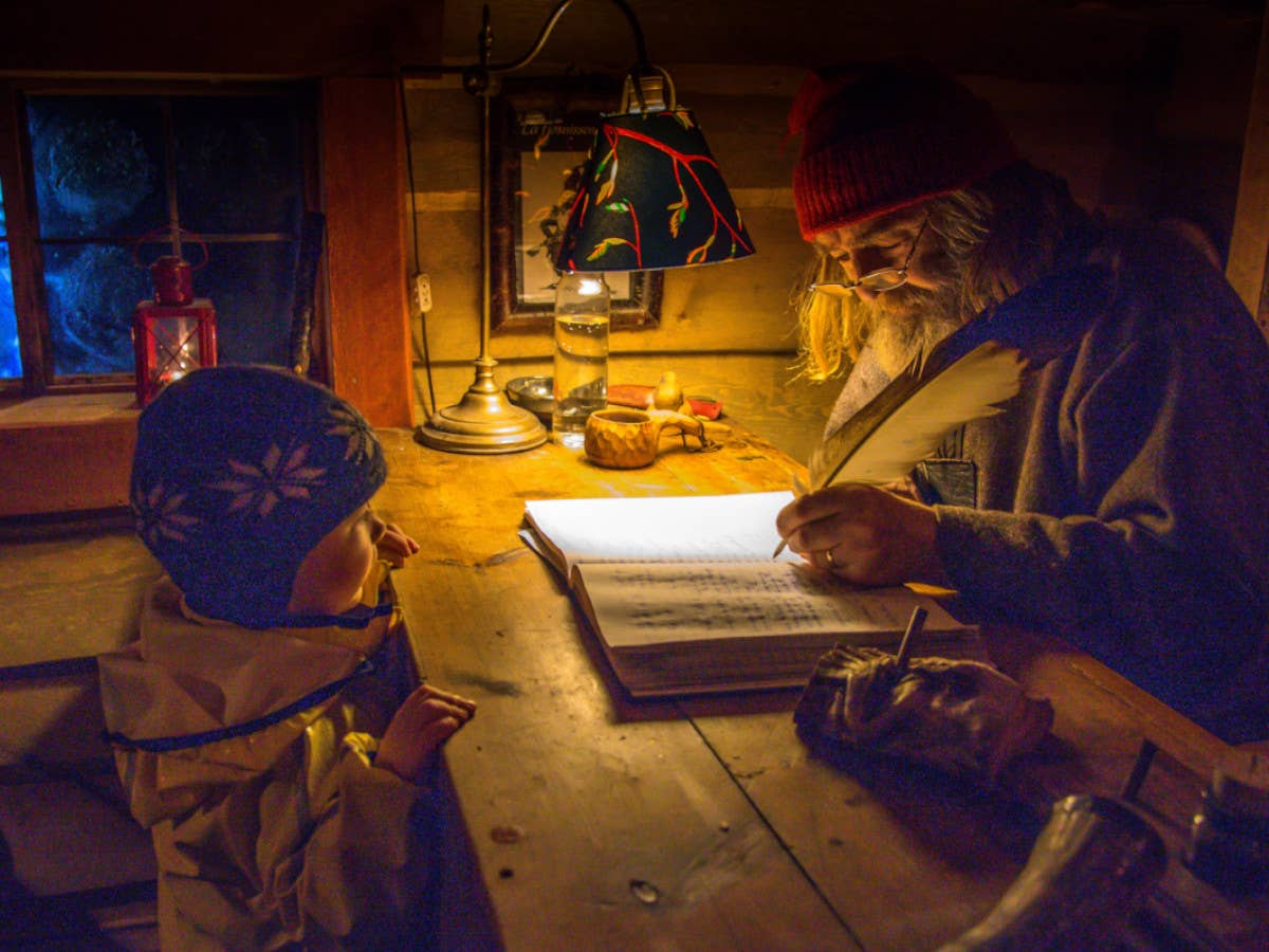 Der Nikolaus schreibt etwas auf ein Blatt Papier, während ein kleiner Junge vor seinem Schreibtisch steht.