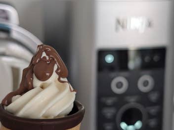 Im Vordergrund (scharf) ein Softeis mit Schoko-Topping, im Hintergrund (unscharf) eine Ninja-Eismaschine