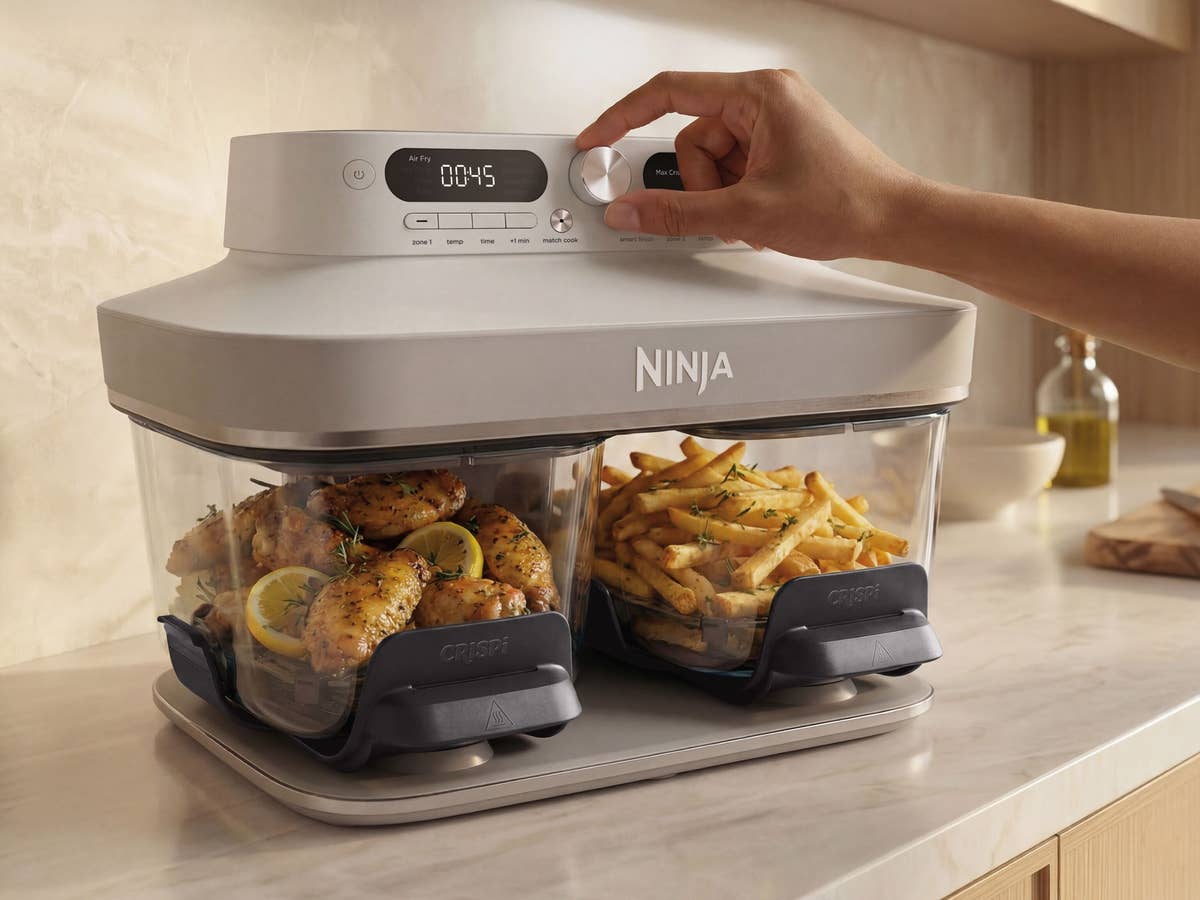 Die Crispi DualZone ist die neueste Erfindung von der Hype-Marke Ninja. Ninja Crispi DualZone Heißluftfritteuse gefüllt mit Pommes und Hähnchen, eine Hand bedient das Gerät und dreht den großen Regler zwischen den beiden Displays