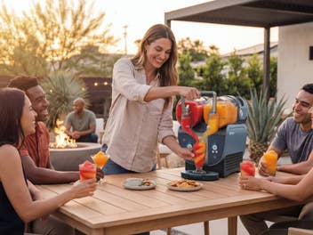 mehrere Personen sitzen im Garten auf der Terasse und trinken Slush-Eis aus der Ninja SLUSHi Twist