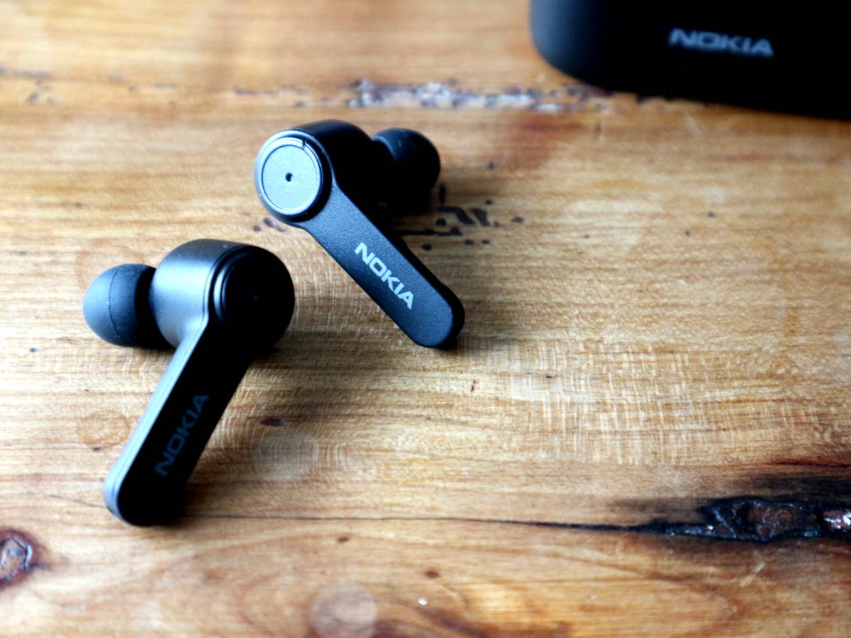 Die Nokia Noise Cancelling Earbuds einzeln vor dem Ladecase auf einem Holztisch.