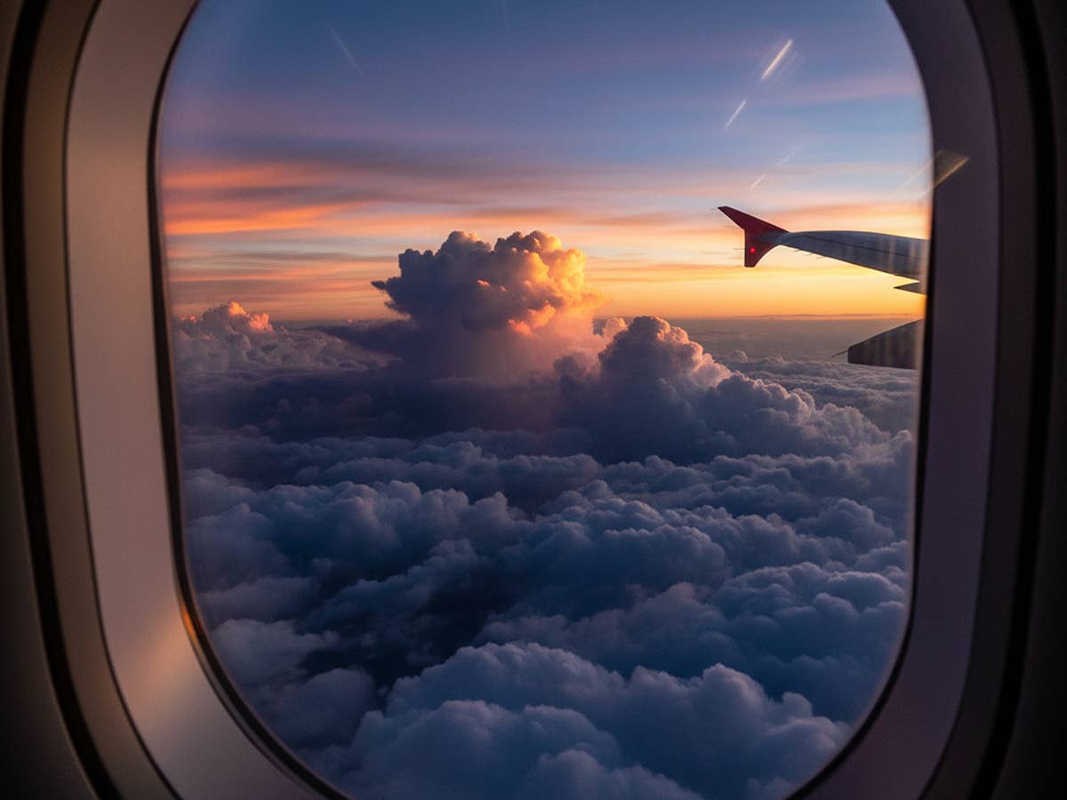 Blick aus dem Fenster eines Flugzeugs auf Wolken im Sonnenuntergang.