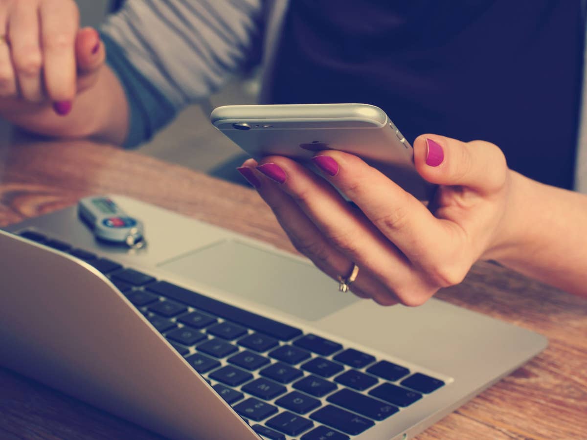 EIn Laptop steht auf einem Tisch, eine Frau hält ein iPhone in der Hand