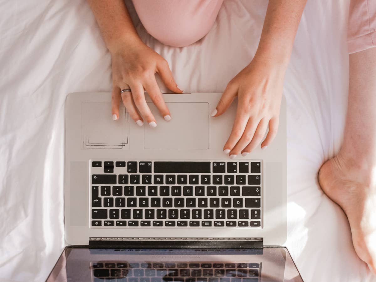 Frau sitzt auf einem Bett am Laptop und betreibt Online Shopping