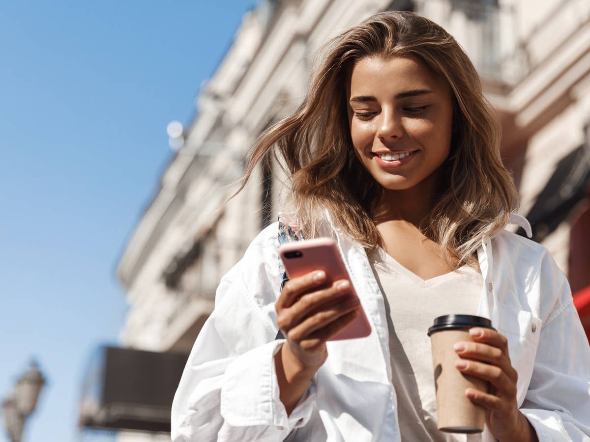 Blonde Frau nutzt ein Smartphone vor blauem Himmel.