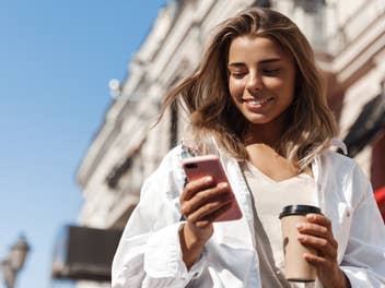 Blonde Frau nutzt ein Smartphone vor blauem Himmel.