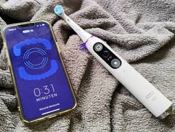 Oral B iO 9N liegt auf einem Handtuch neben einem Smartphone mit geöffneter Oral-B App.