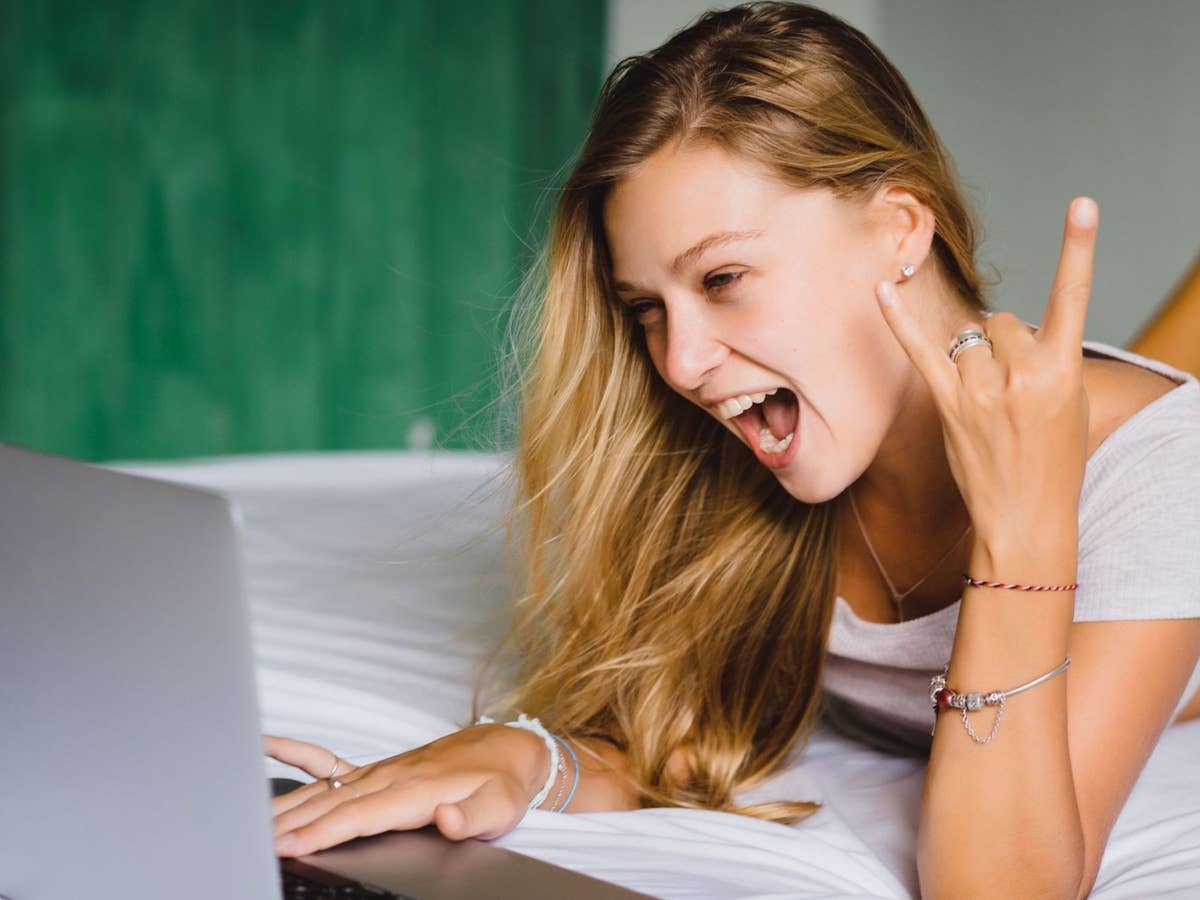 Frau liegt auf dem Bett und schaut in einen Laptop