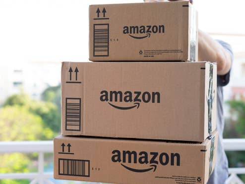 Person hält drei Amazon-Pakete in den Händen und trägt sie in die Wohnung