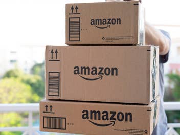 Person hält drei Amazon-Pakete in den Händen und trägt sie in die Wohnung