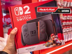 Person hält im Laden Nintendo Switch 2 in der Hand, daneben das MediaMarkt-Logo