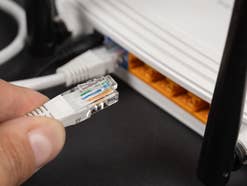Person steckt LAN-Kabel in den Router