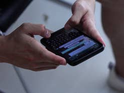 Eine Person hält ein Handy in den Händen, auf dem ein WhatsApp-Chat geöffnet ist.